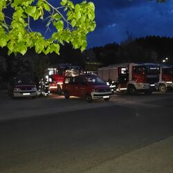 In einer nächtlichen Szene stehen mehrere Feuerwehrfahrzeuge auf einem Parkplatz, während Einsatzkräfte Geräte wegräumen.