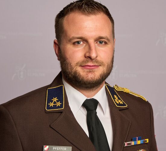Dominic Pfeffer trägt eine Uniform mit Abzeichen, posiert vor einem neutralen Hintergrund | © Name.