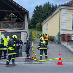 Feuerwehrleute bereiten sich auf einen Einsatz vor einem Gebäude mit einem Einsatzfahrzeug und Wasserschlauch vor.