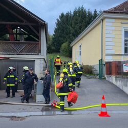 Feuerwehrleute bereiten sich am Einsatzort vor, während ein Feuerwehrfahrzeug und Schläuche in der Nähe stehen.