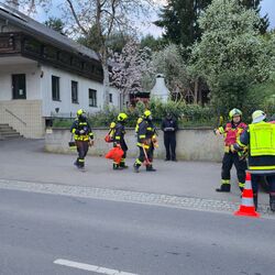 Feuerwehrleute in Schutzkleidung besprechen sich vor einem Einsatzfahrzeug neben einem Wohngebäude.