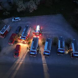 Mehrere Feuerwehrfahrzeuge stehen im Dunkeln, während Einsatzkräfte sich um die Fahrzeuge versammeln.