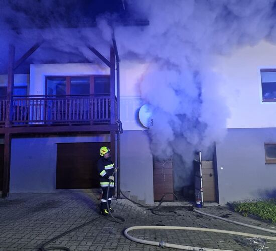Rauch, der aus einem Haus dringt, während ein Feuerwehrmitglied einen Schlauch hält.