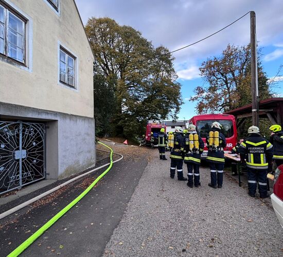 Feuerwehrleute in Schutzkleidung bereiten sich neben einem Gebäude mit Schläuchen und Einsatzwagen auf einen Einsatz vor.