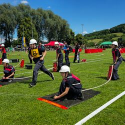Jugendliche in Feuerwehruniformen nehmen an einem Wettkampf auf einem grünen Feld teil. | © Name