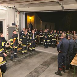 Feuerwehrmitglieder stehen in einer Fahrzeughalle während der Übungs-Nachbesprechung.