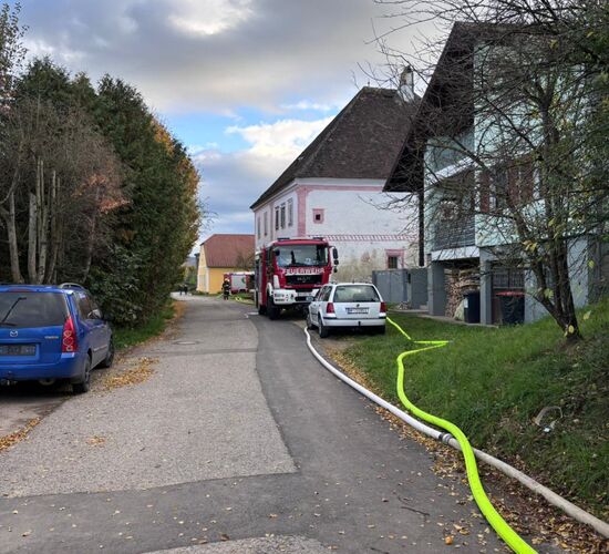 Ein Feuerwehrfahrzeug steht in einer ländlichen Straße, während Schläuche für einen Einsatz ausgerollt sind.